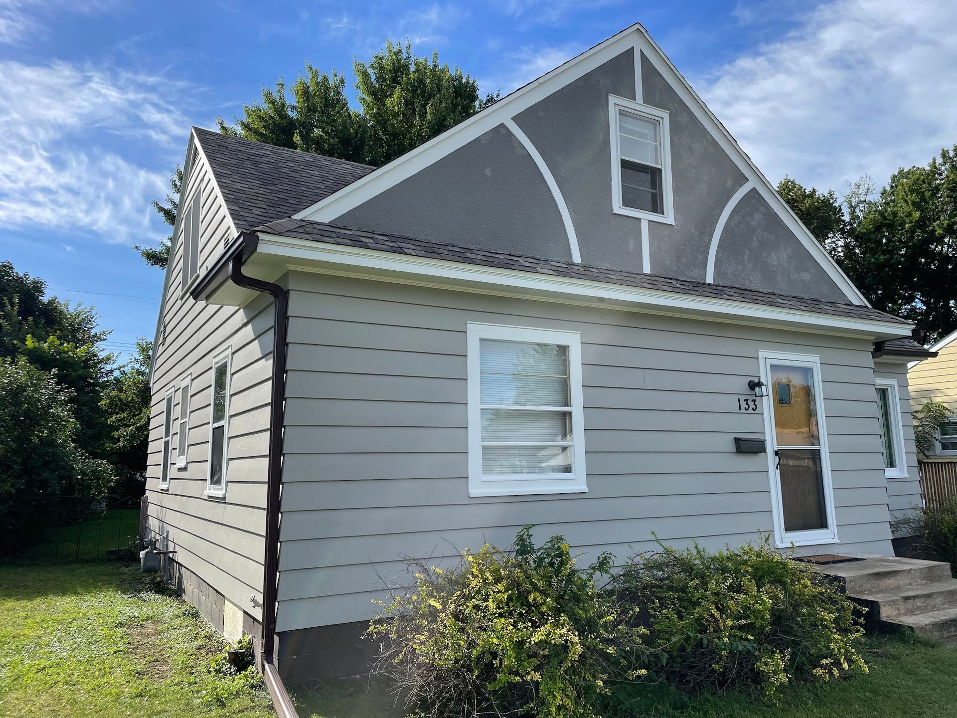 Gray house with a dark roof and white trim under a blue sky.