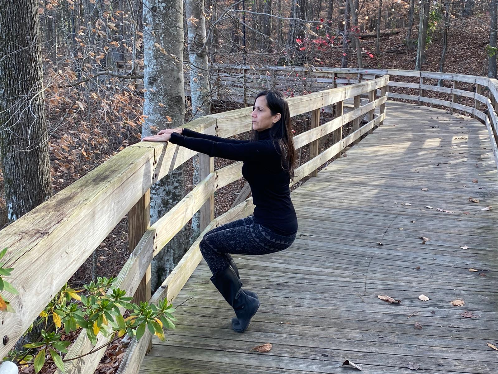 A woman is squatting on a wooden bridge in the woods.