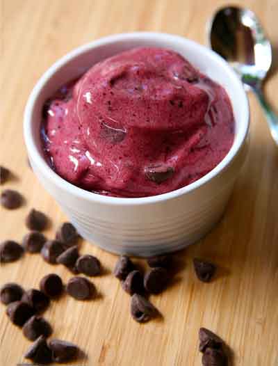A bowl of ice cream with chocolate chips and a spoon on a wooden table.