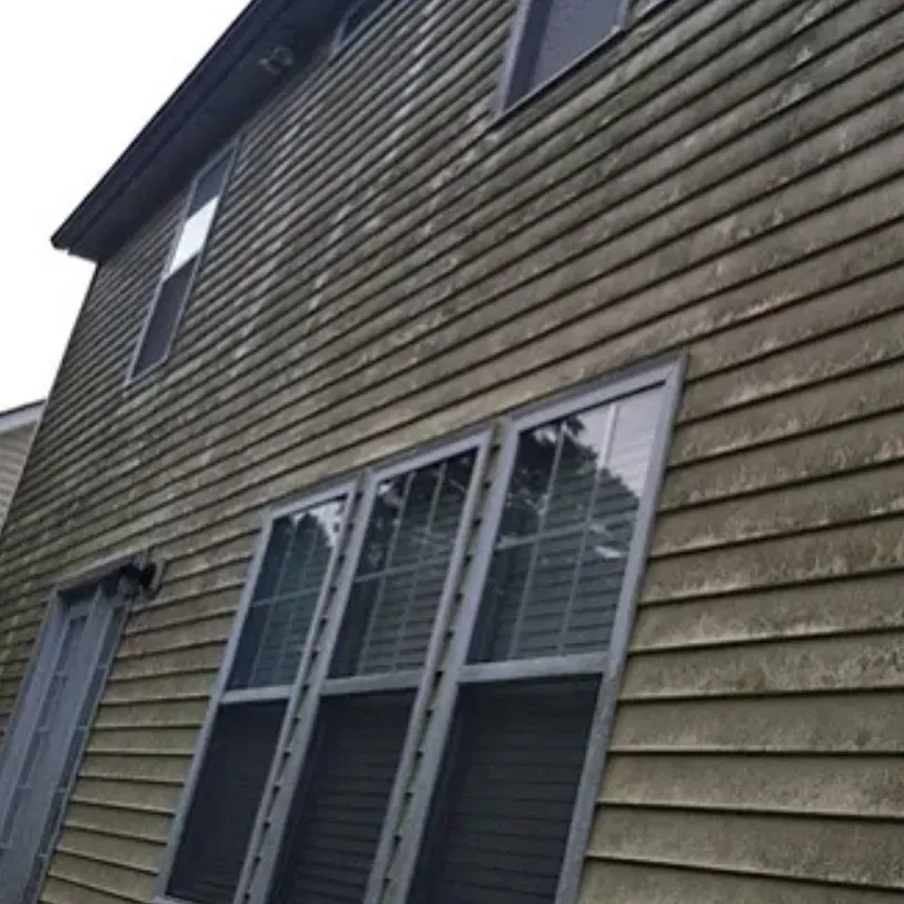 Two-story house with weathered, gray siding and windows.