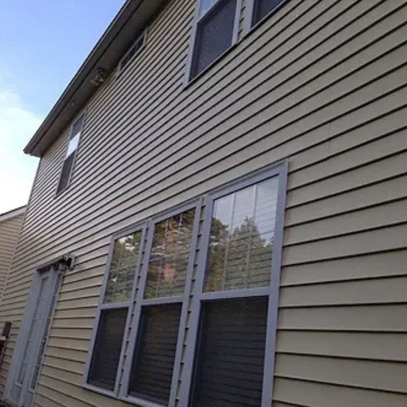 Beige sided house with multiple windows; blue sky in background.