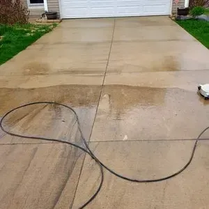 A wet concrete driveway with a black hose and a garage door, freshly cleaned.