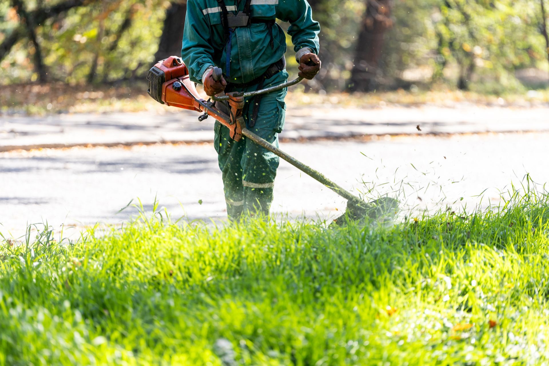 Person in green work suit using a weed whacker on green grass.