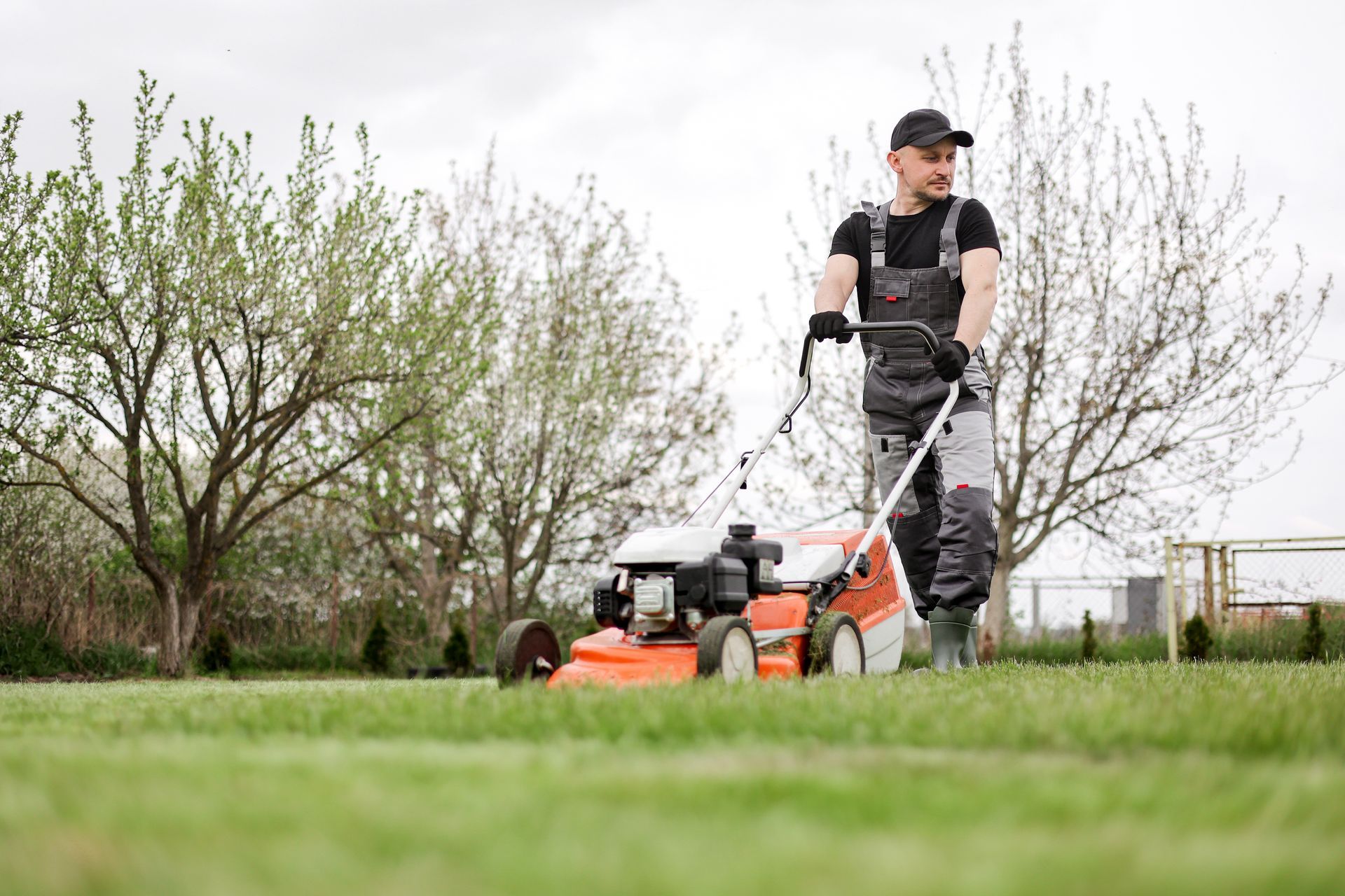 Man mowing a green lawn with an orange lawnmower outdoors.