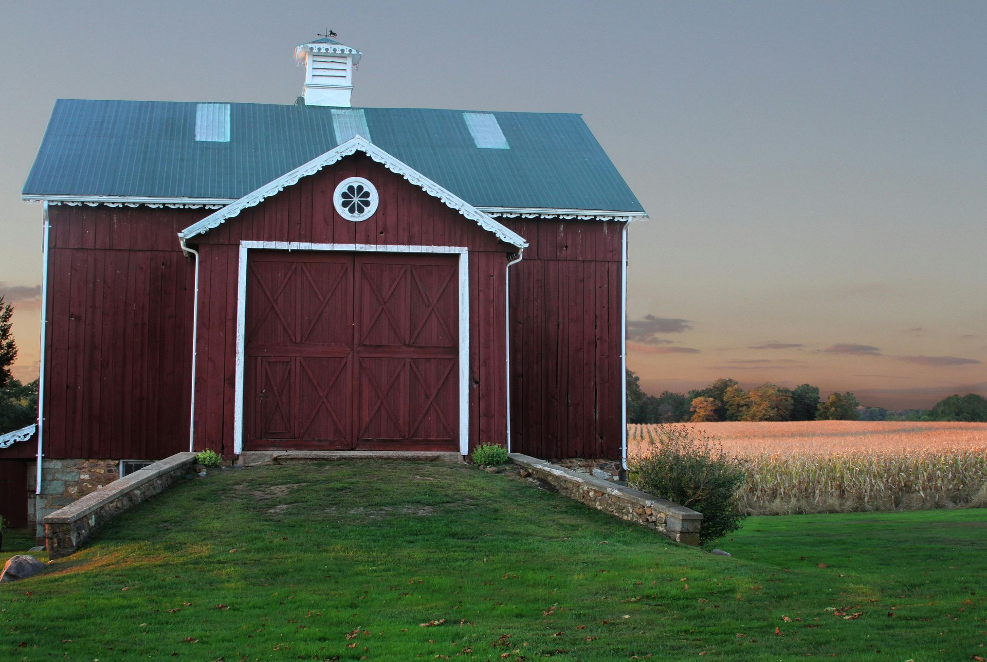 A red barn with a blue roof is in the middle of a grassy field.