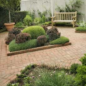 Urban small garden with brick patio, wooden bench and potted plants.