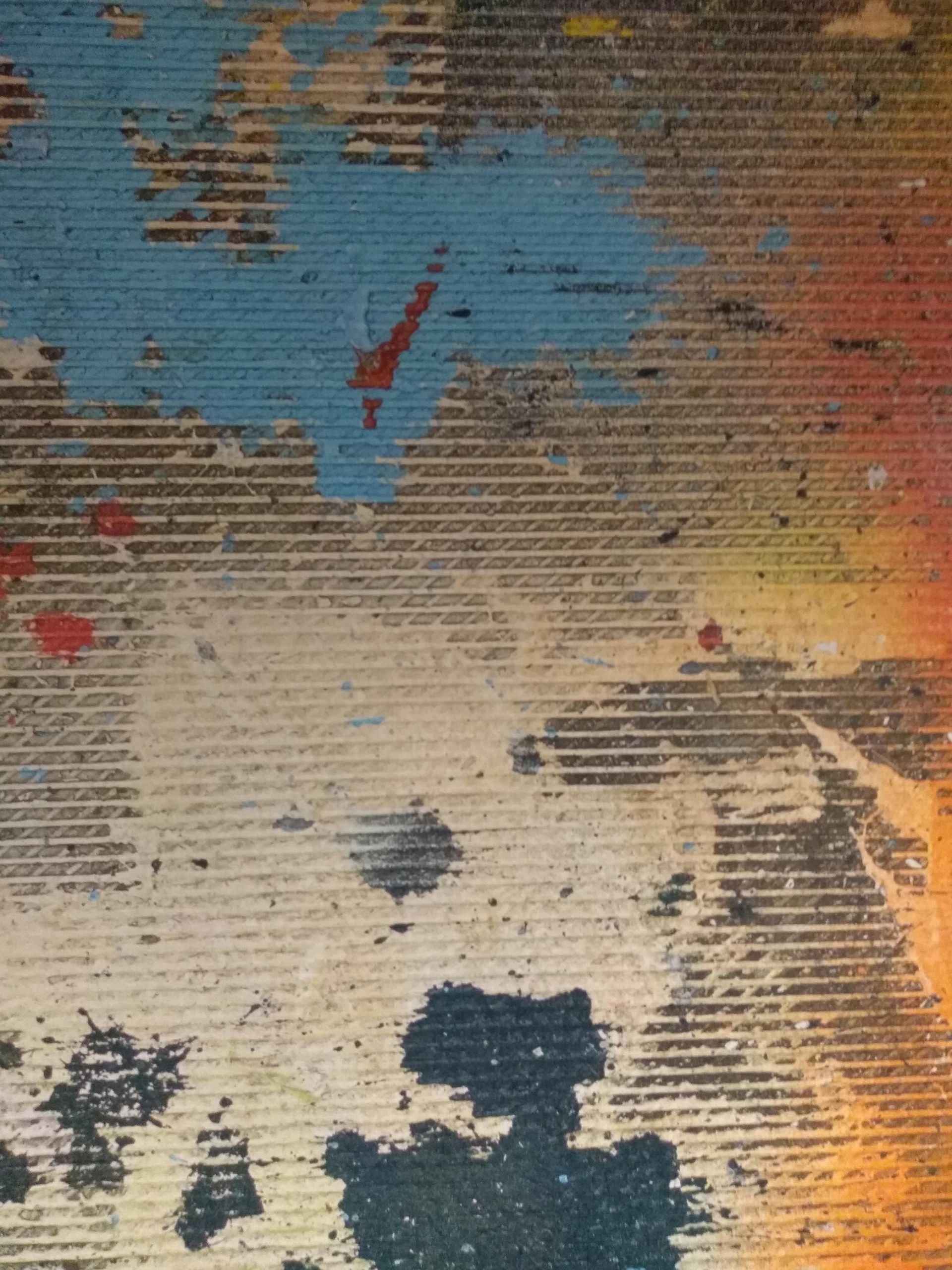 Abstract art on textured, corrugated surface. Splashes of blue, orange, red, and black paint.