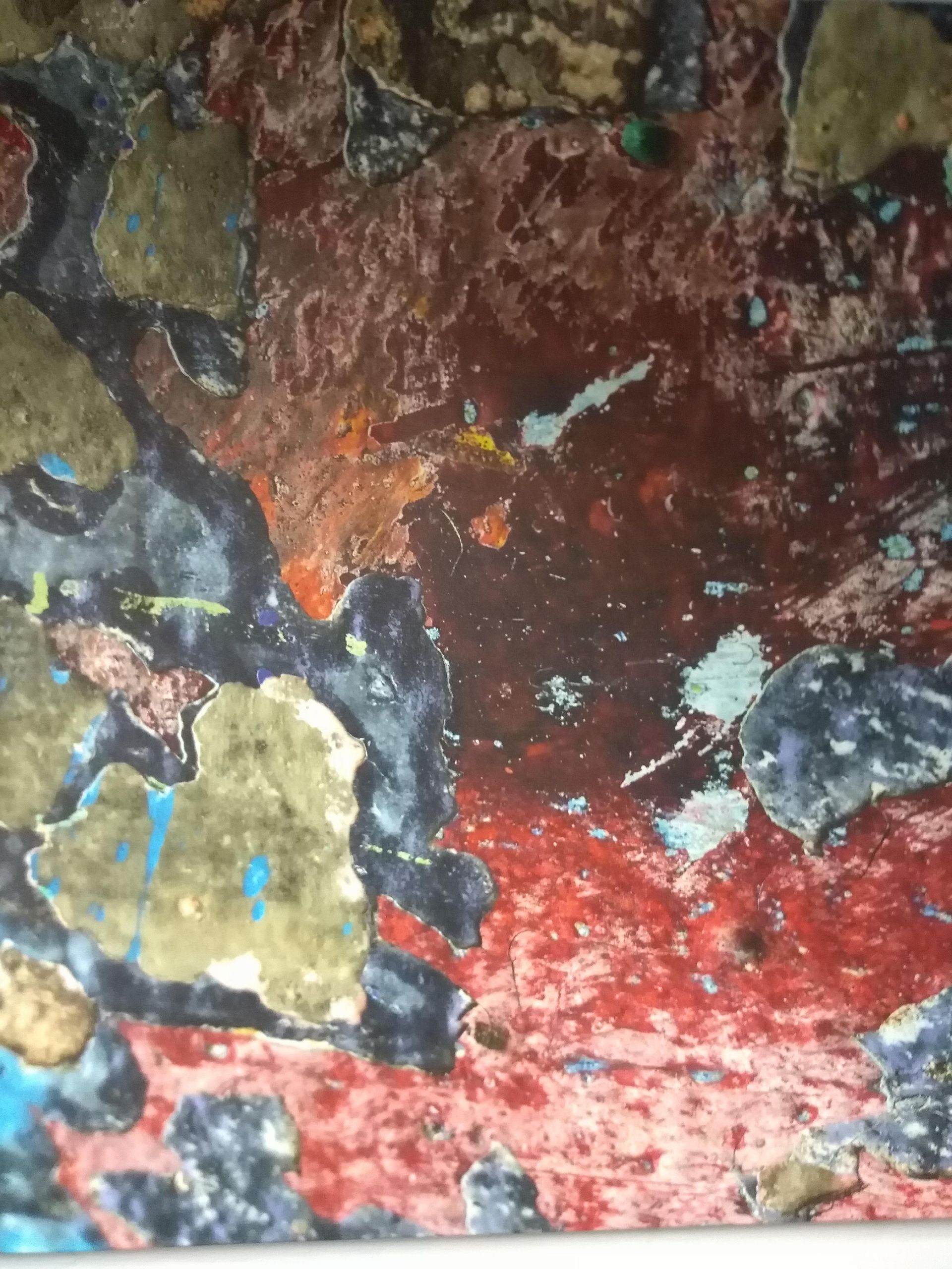 Abstract, textured surface with patches of red, brown, black, blue, and green.