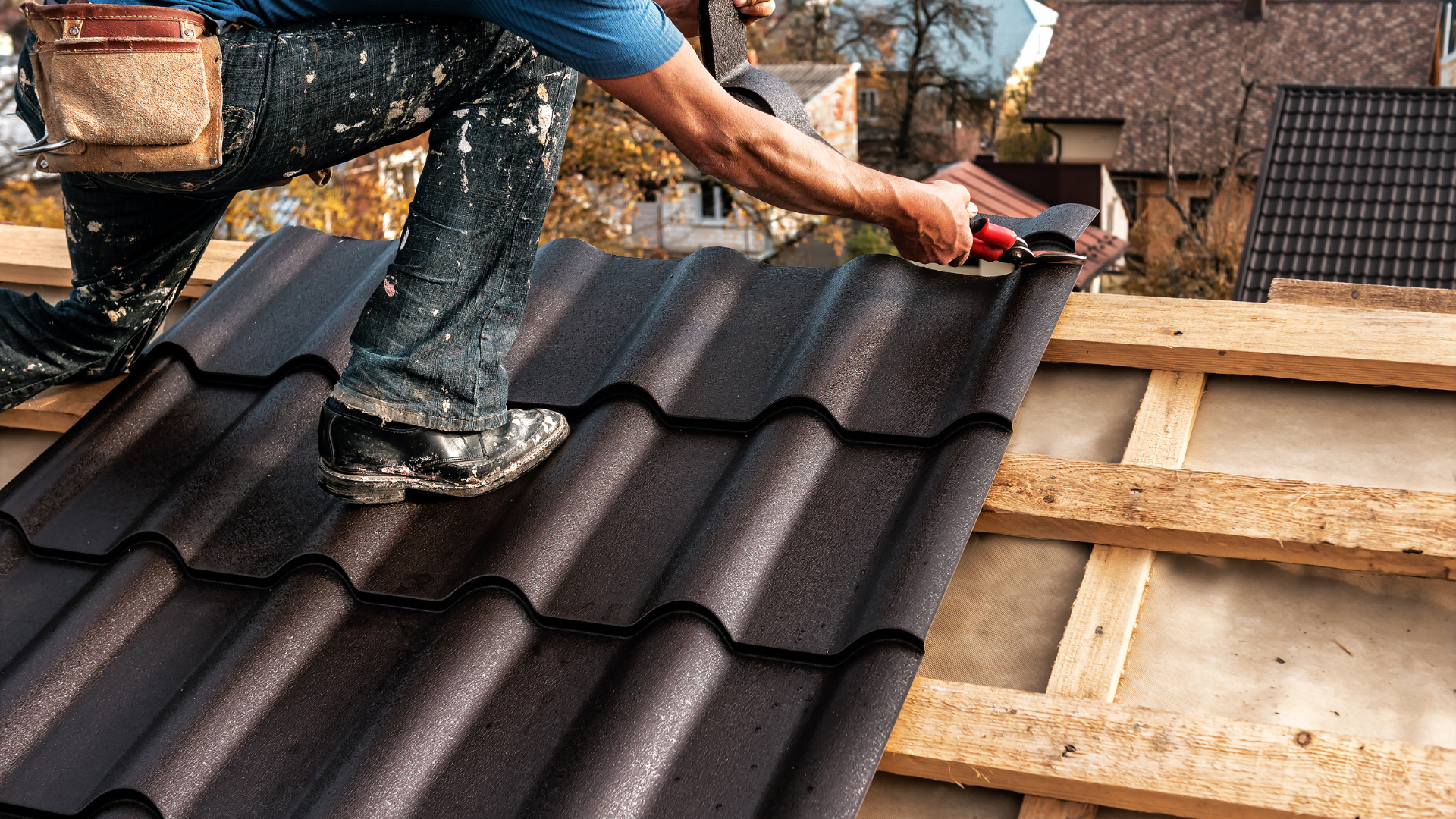 Worker installing dark roof tiles on a house under construction