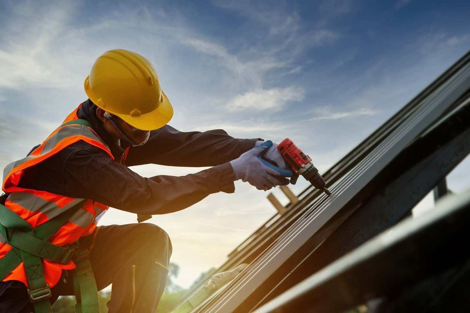 Worker in yellow hard hat inspecting roof shingles with tools nearby