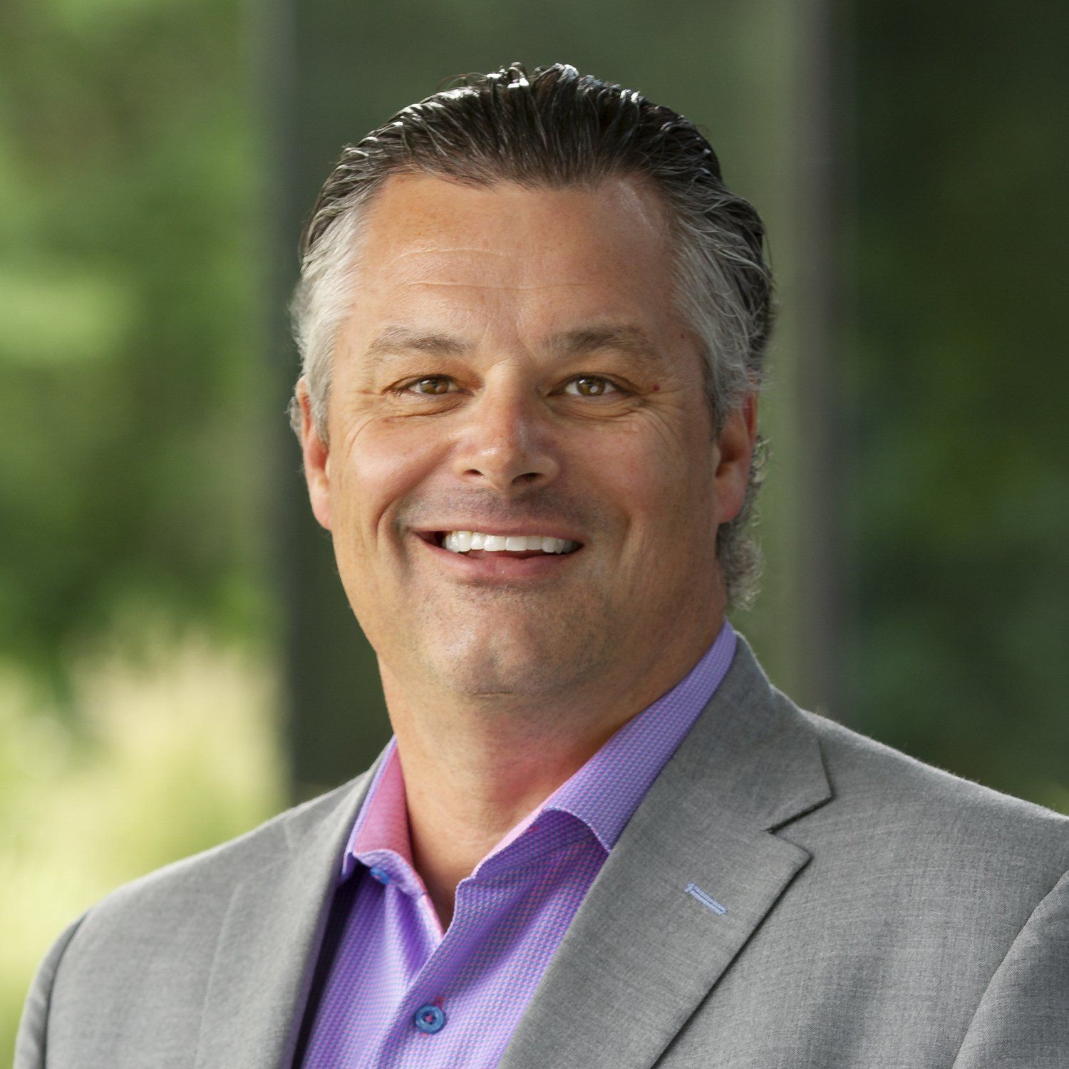 A man in a suit and purple shirt is smiling for the camera. kyle didier