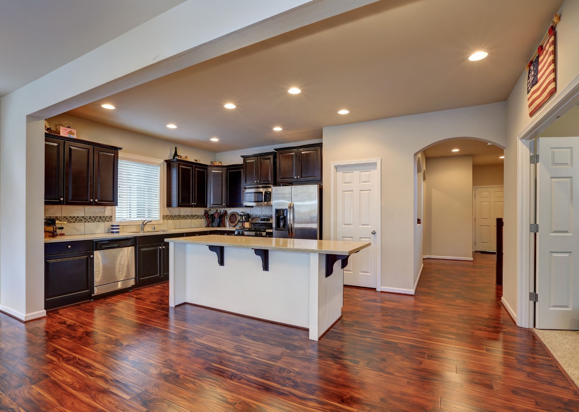 Spacious kitchen with dark cabinets, stainless steel appliances, a white island, and hardwood floors.