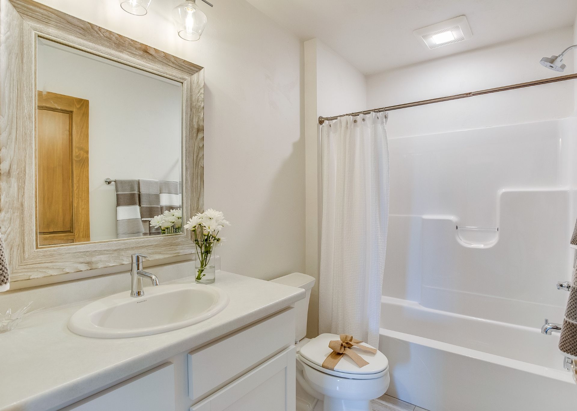 Bathroom with white walls, vanity, bathtub/shower, toilet, and decorative mirror.