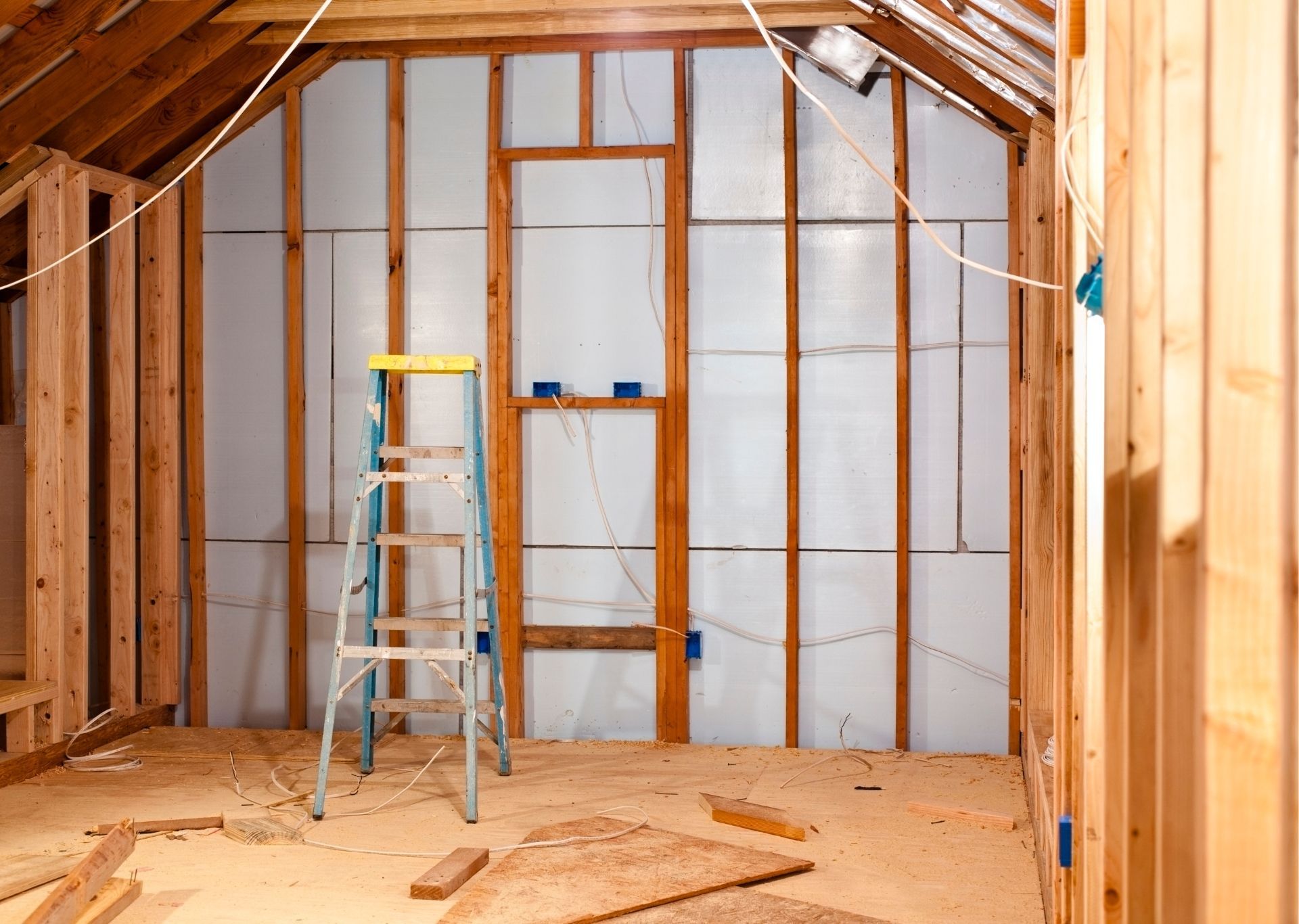Interior of a room under construction with wood framing and insulation. A ladder is positioned against the wall.