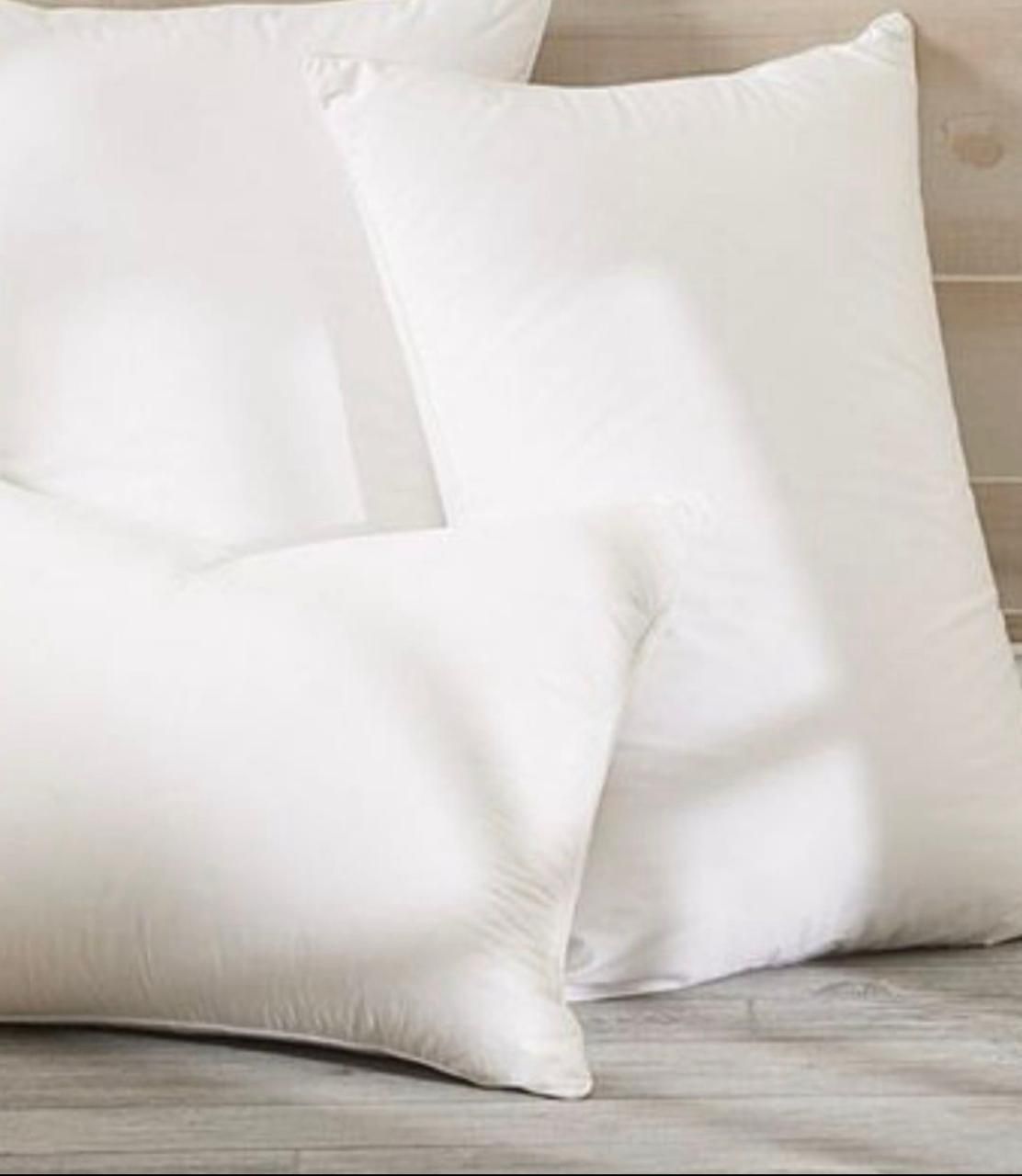 Almohadas blancas y grises cuidadosamente dispuestas sobre una cama beige en un dormitorio con iluminación tenue.