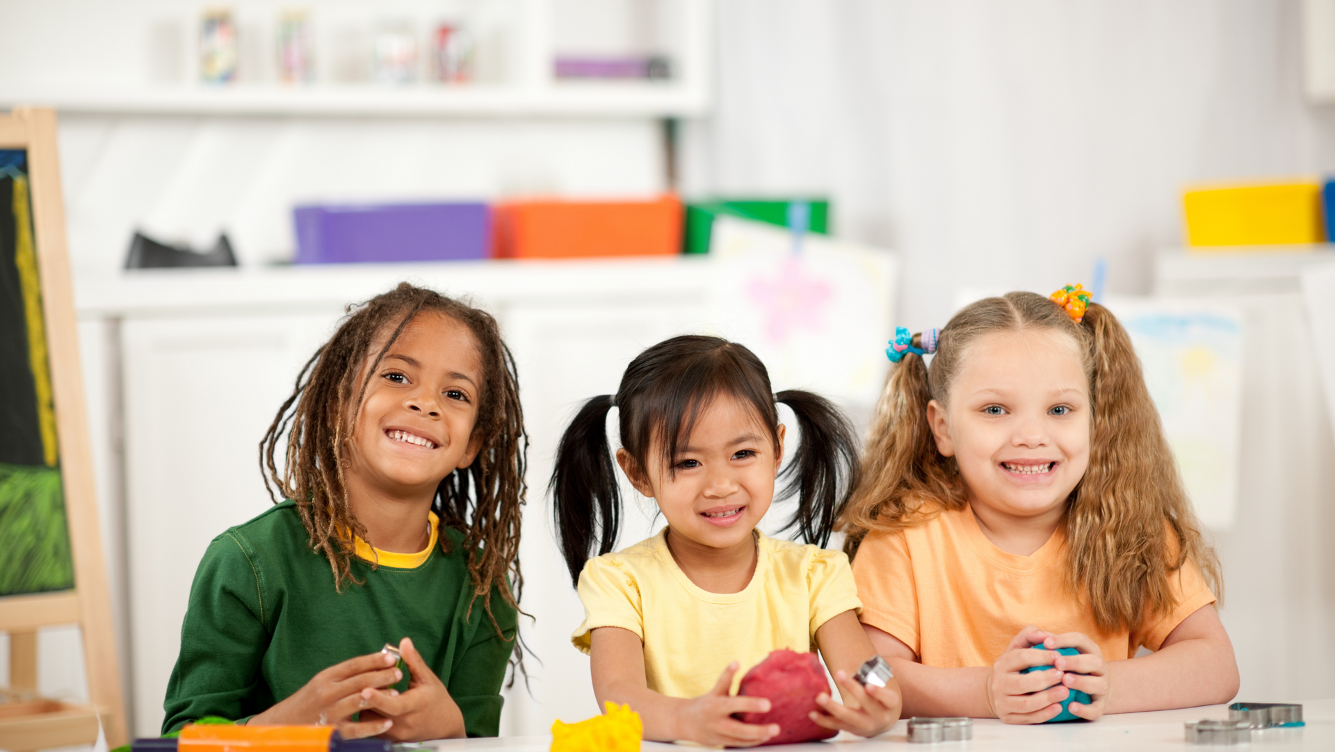 Three young girls are sitting at a table playing with clay.