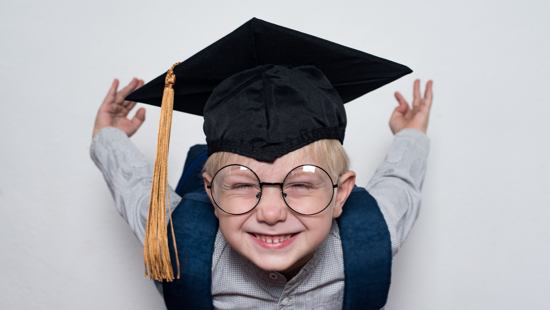 A young boy wearing a graduation cap and gown and glasses.