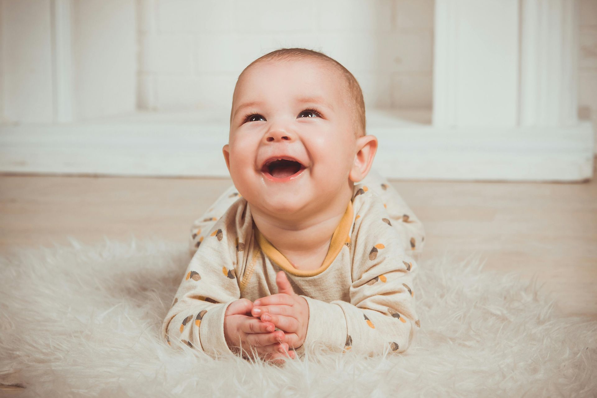 A baby is laying on its stomach on a white rug and smiling.