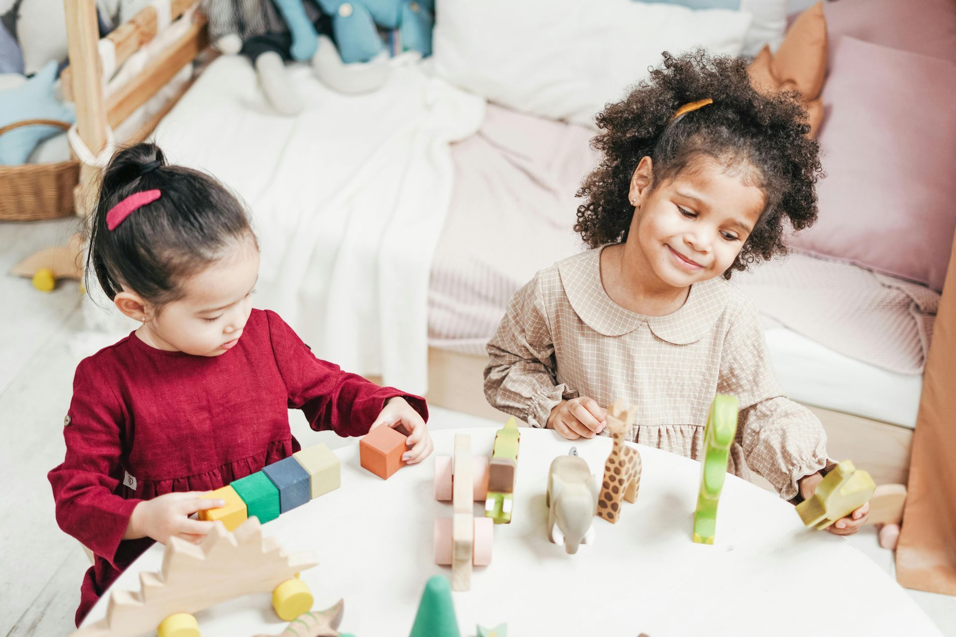 Two little girls are playing with wooden blocks at a table.