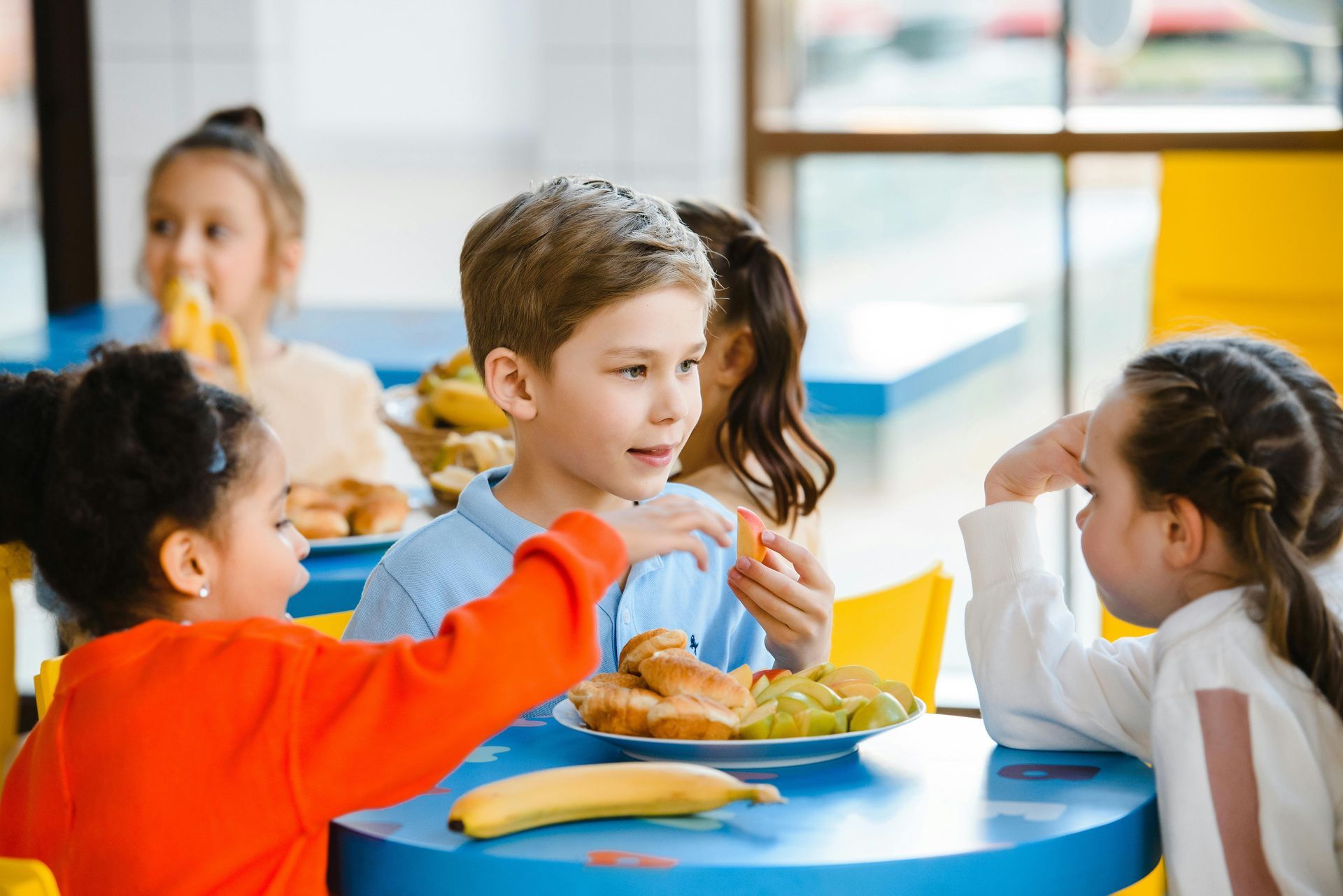 A group of children are sitting at a table eating food.