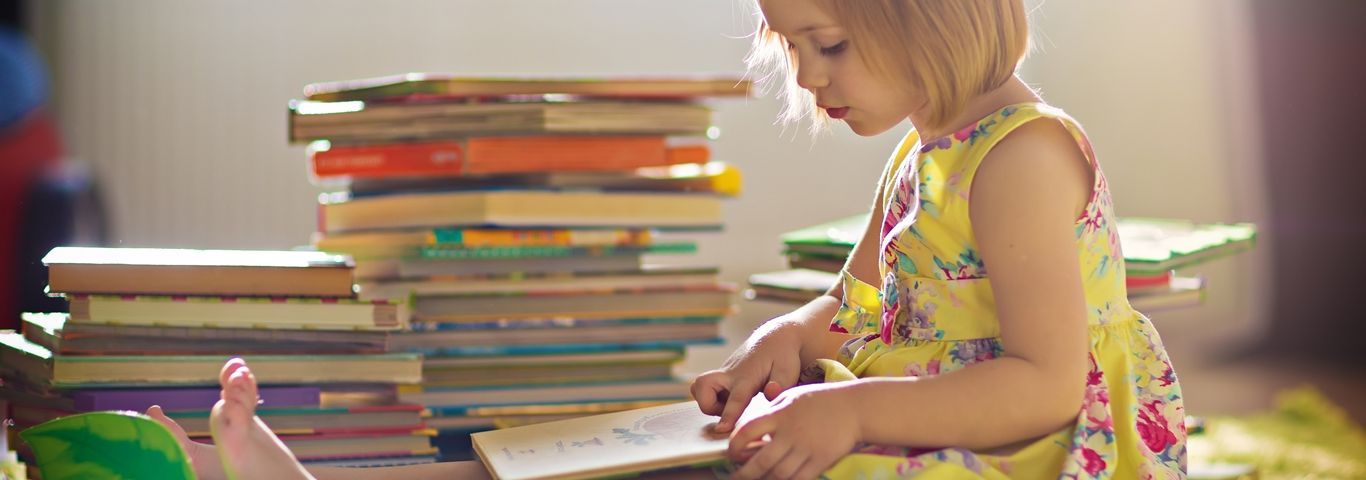 A little girl is sitting on the floor reading a book.