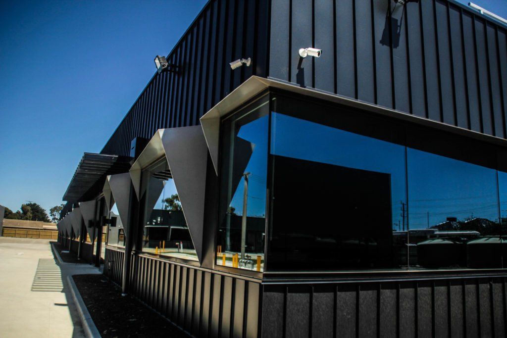 Image depicts a new modern commercial building with beautiful tinted black windows, aluminium sills and black Architecturally Designed Panel System (APS) finishing.