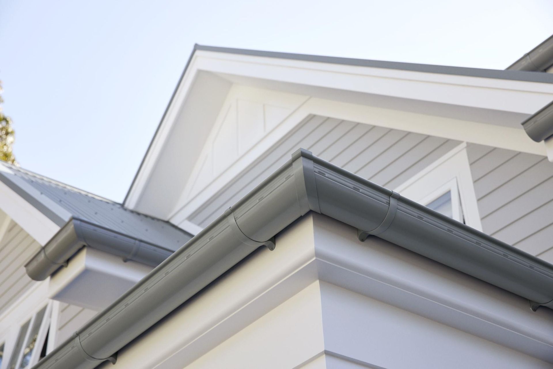 Taken from the ground up, the image depicts a grey coloured double story weather board home. The image captures the corners and roof pitches highlighting the new grey Colourbond guttering system and topped off with a blue sky backdrop.