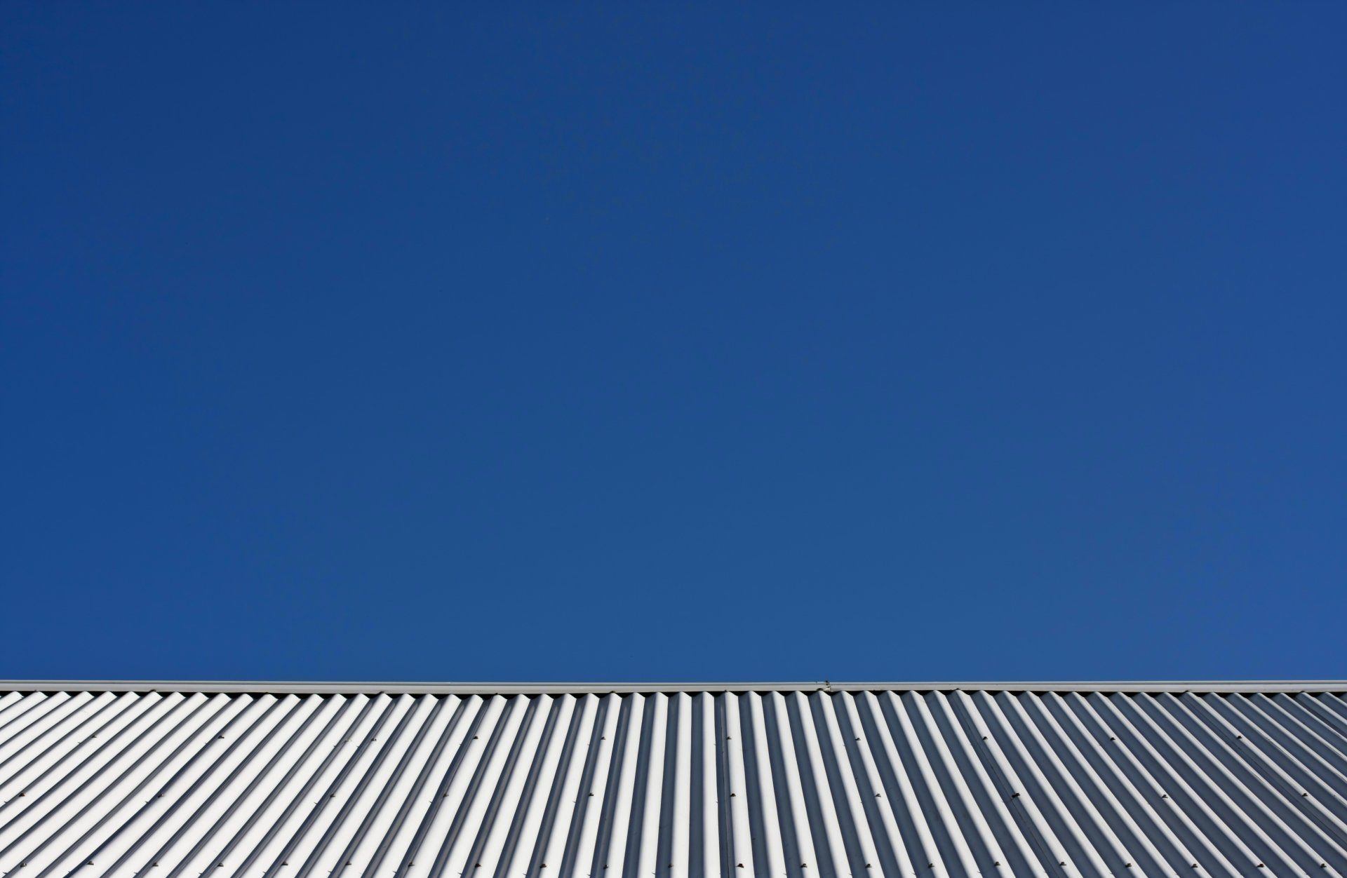 Image depicts a corrugated iron roof, taken from the gutter up to the pitched top with a clear blue sky  in the background.
