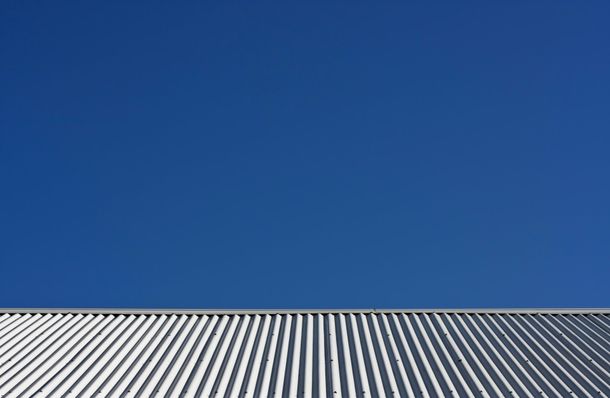 Image depicts a corrugated iron roof, taken from the gutter up to the pitched top with a clear blue sky  in the background.