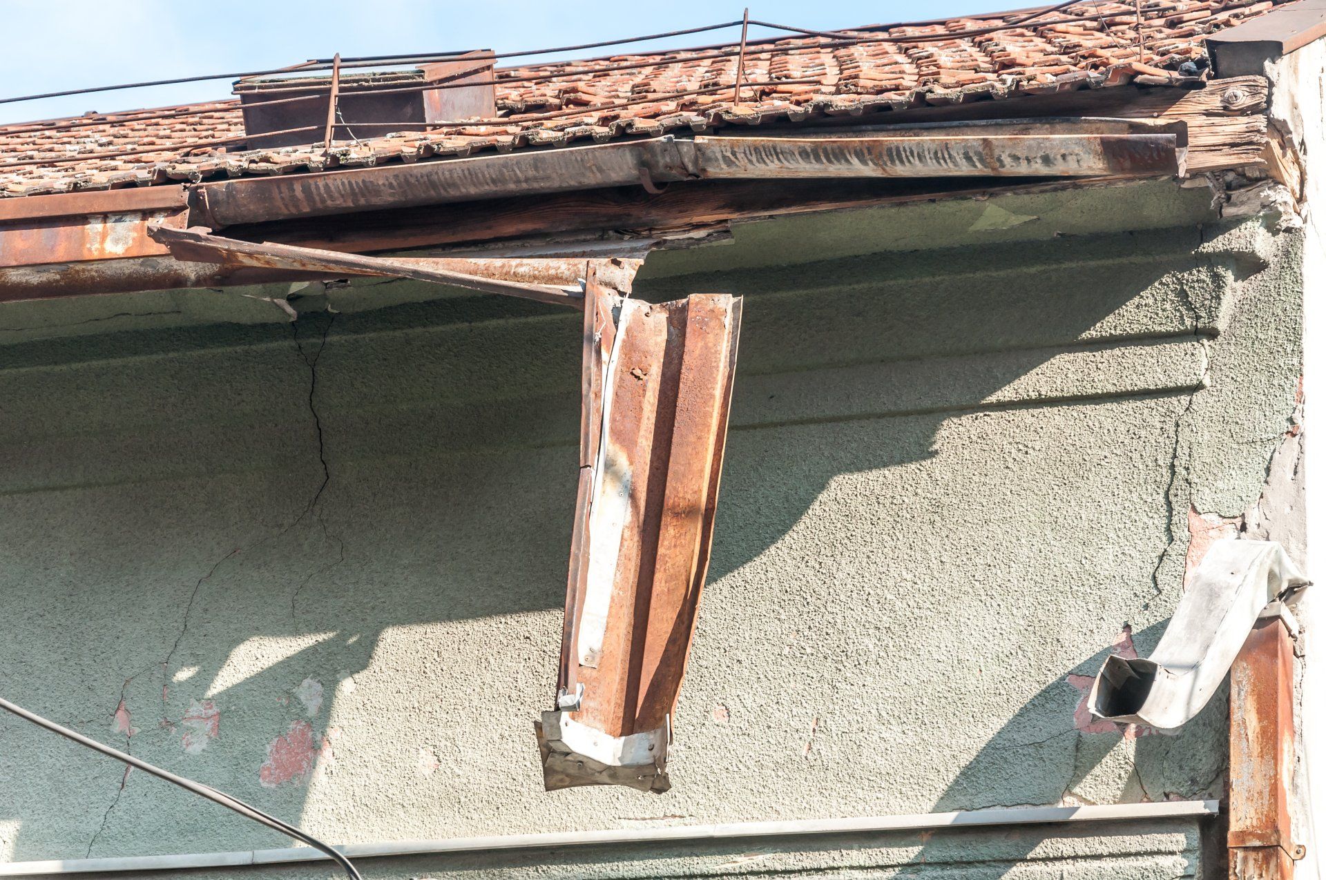 Image depicts a completely destroyed gutter system, partially hanging off  a roof. It appears the guttering is simply old and worn.