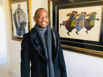 A man in a black coat and scarf is standing in front of a painting.