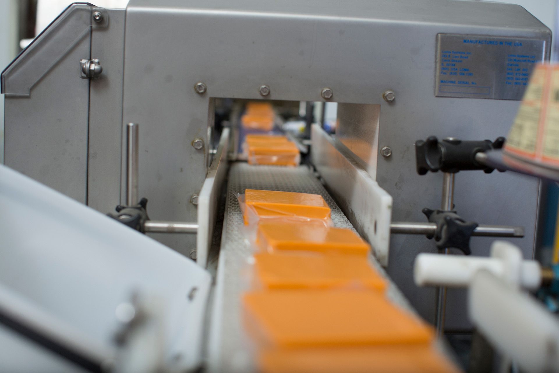 A conveyor belt filled with orange blocks of cheese going through a machine