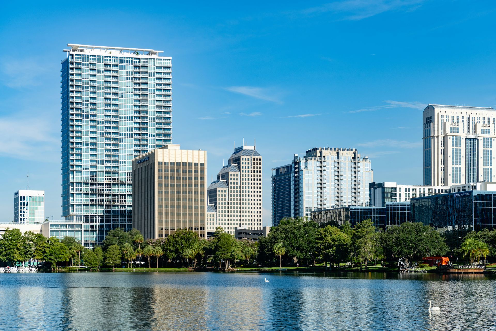 Orlando, Florida skyline: modern high-rise buildings line a waterfront under a bright blue sky.