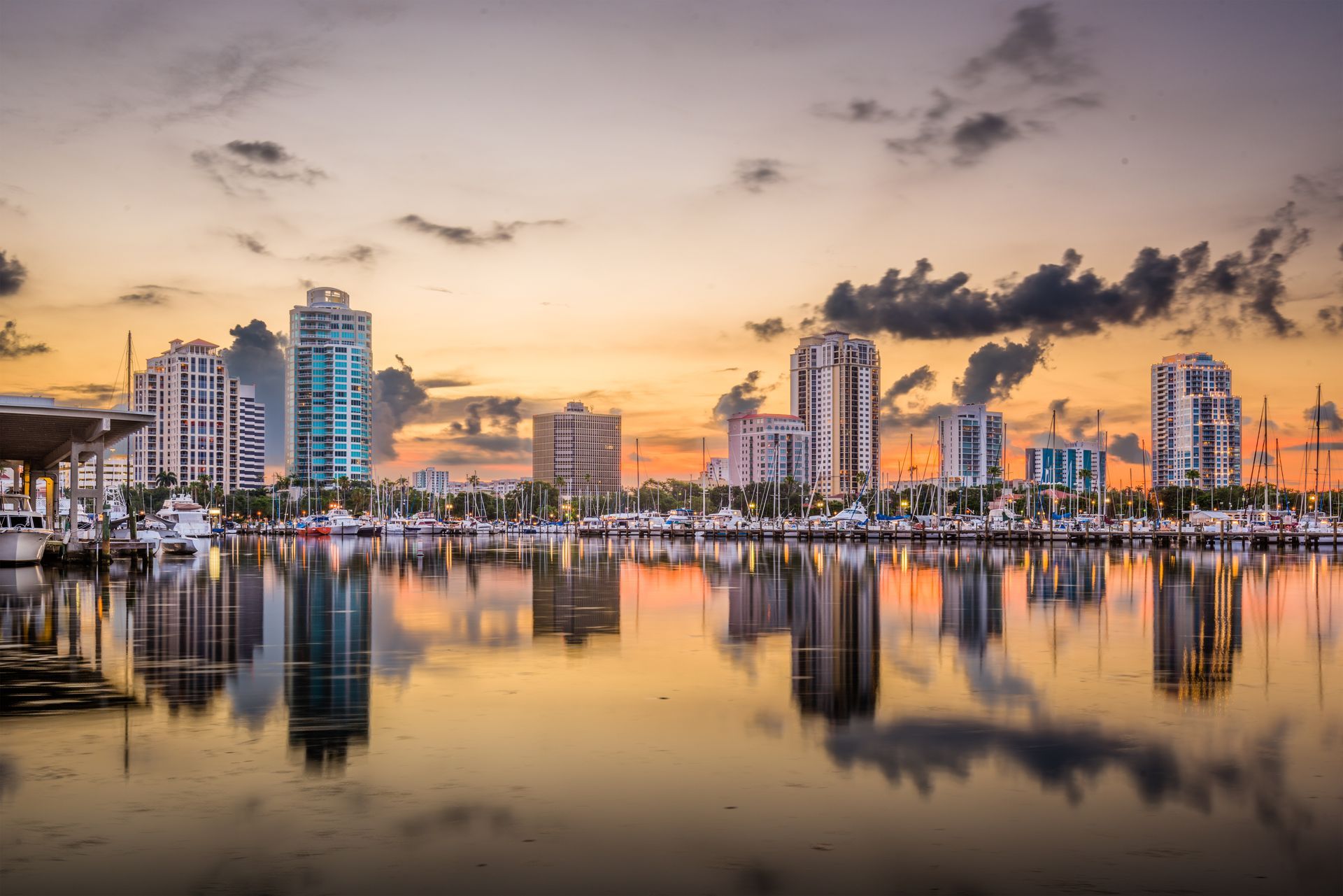 Skyline of St. Petersburg, Florida, reflected in calm water at sunset with orange and pink hues.