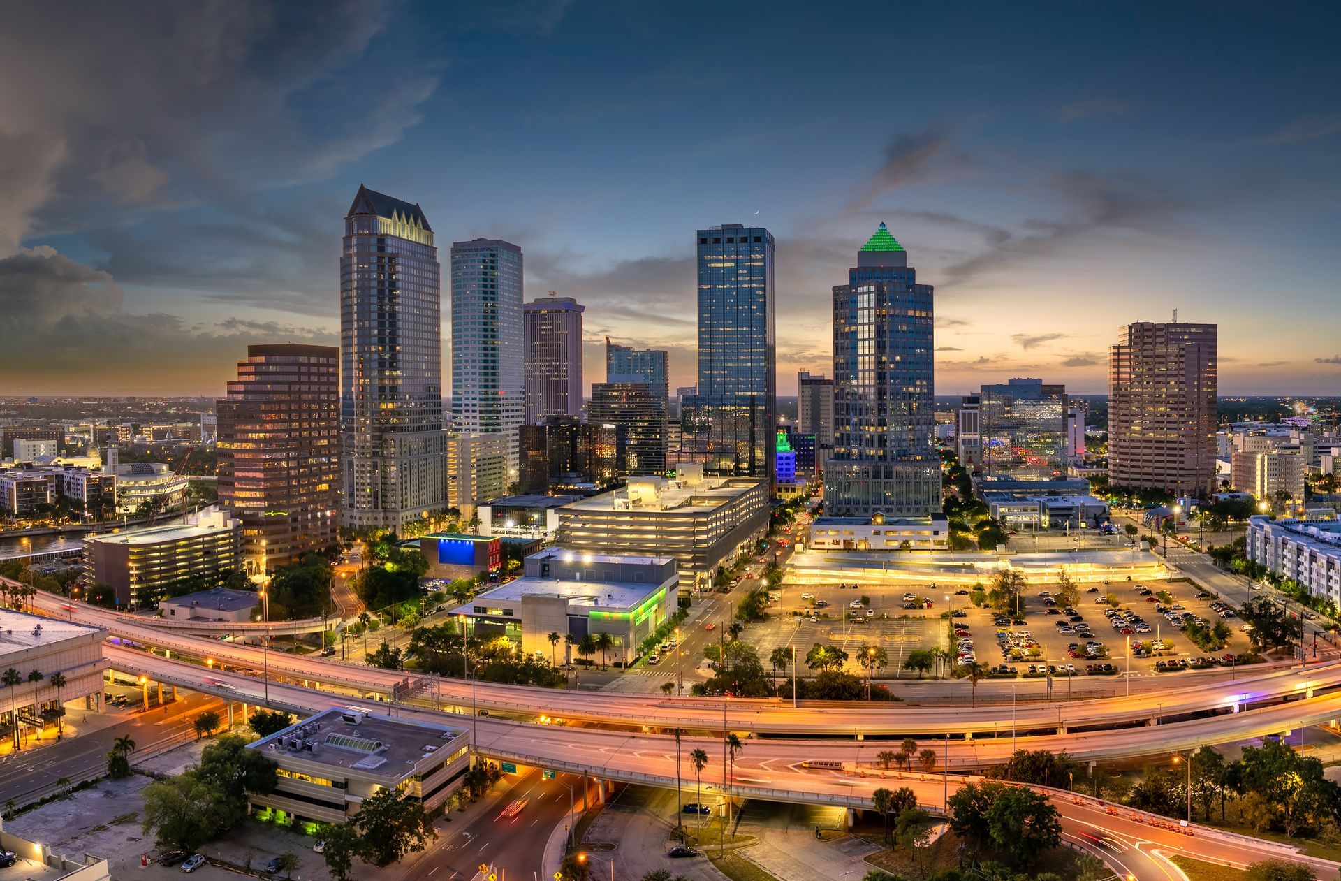 Night view of Tampa, Florida skyline with lit buildings and a blue-toned sky.