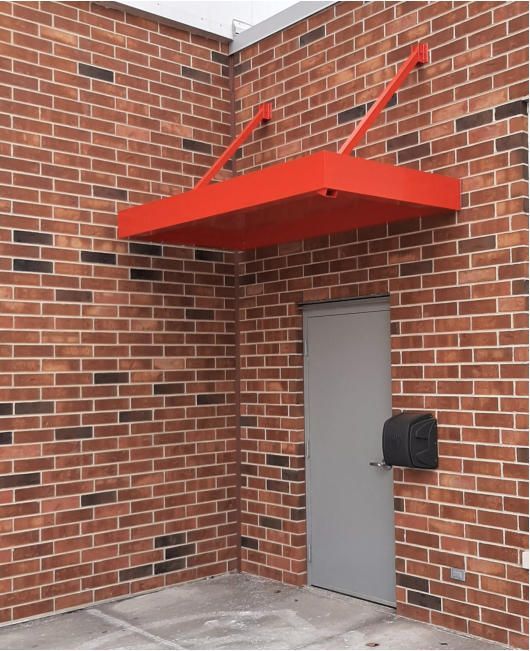 A brick wall with a red canopy over a door and a mailbox.