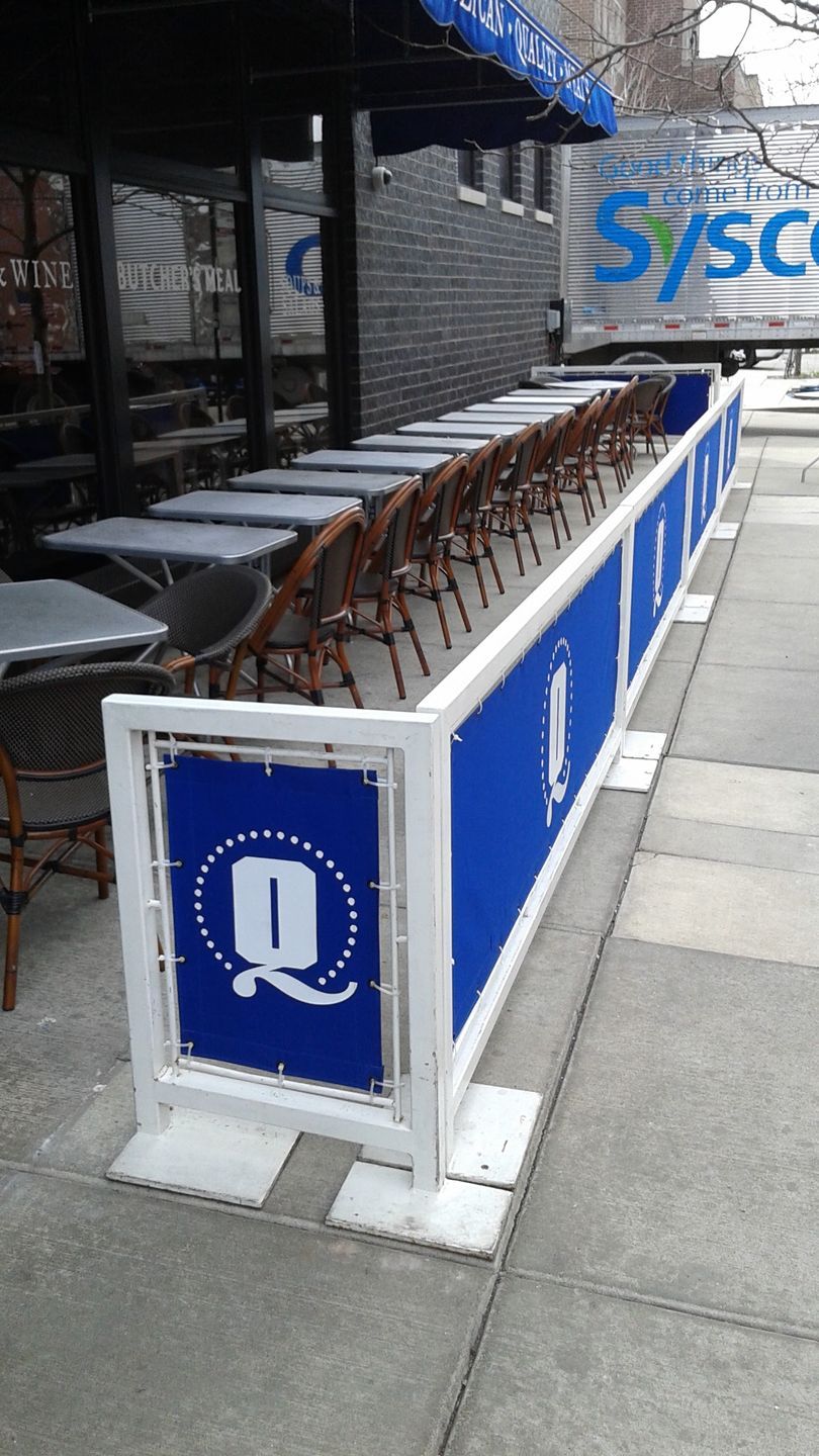 A row of chairs are lined up on a sidewalk next to a blue and white barrier.