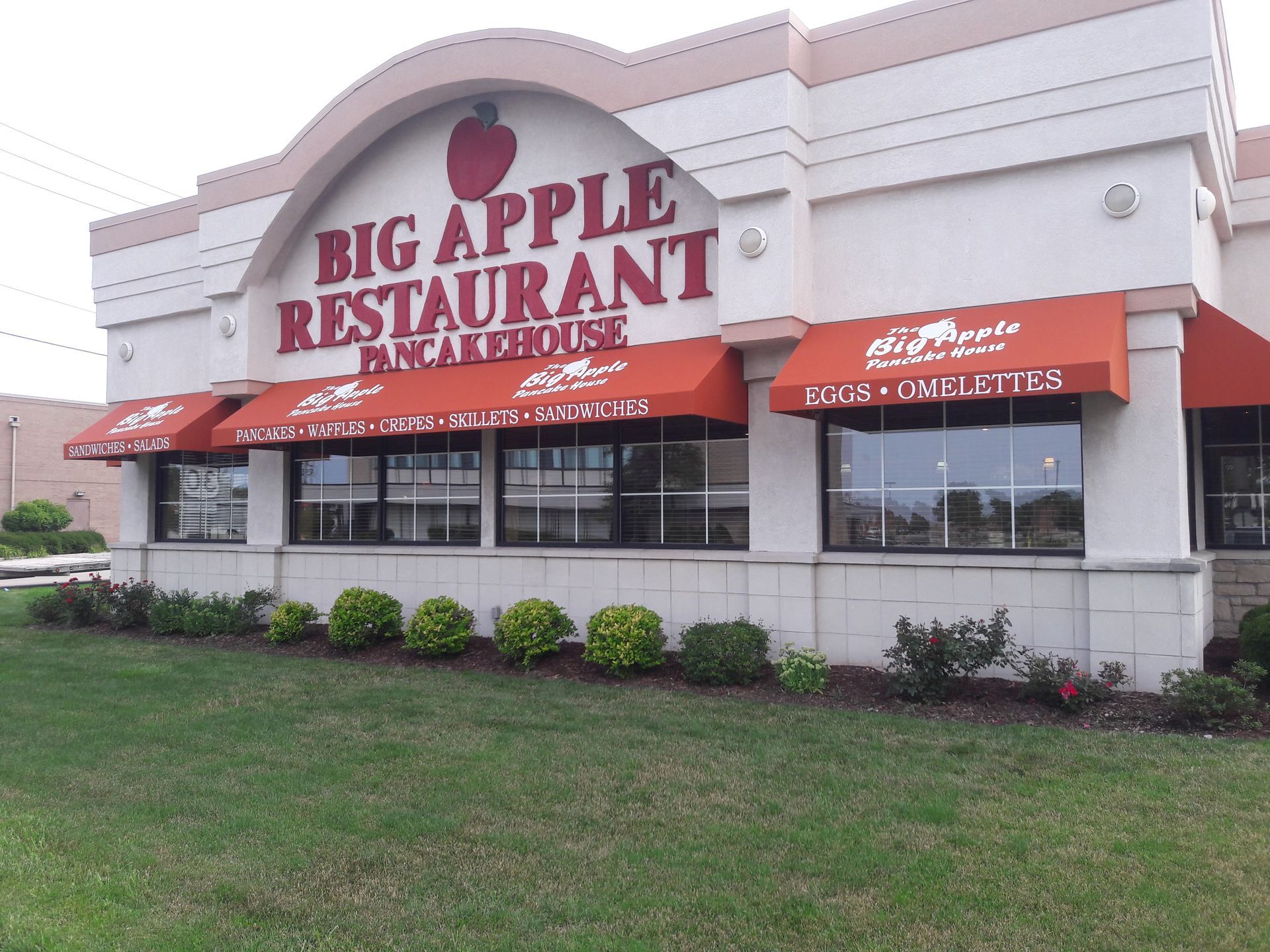 A big apple restaurant with red awnings on the windows
