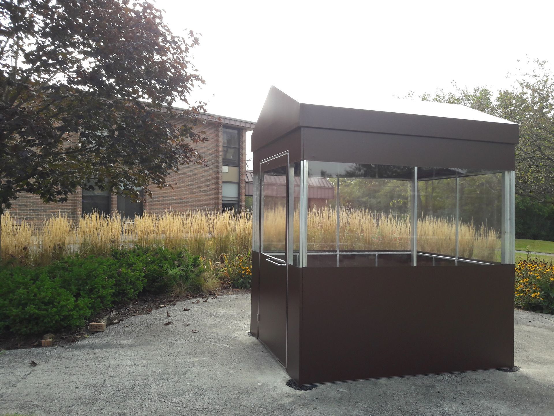 A brown gazebo with a clear roof sits in front of a brick building