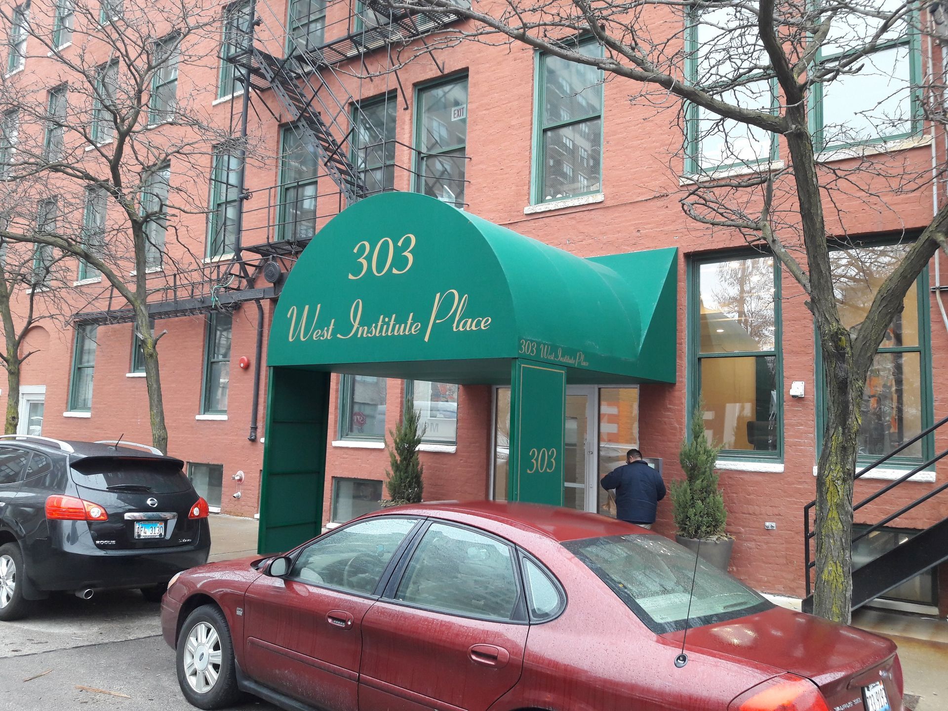 A red car is parked in front of a building that says 303 west institute place