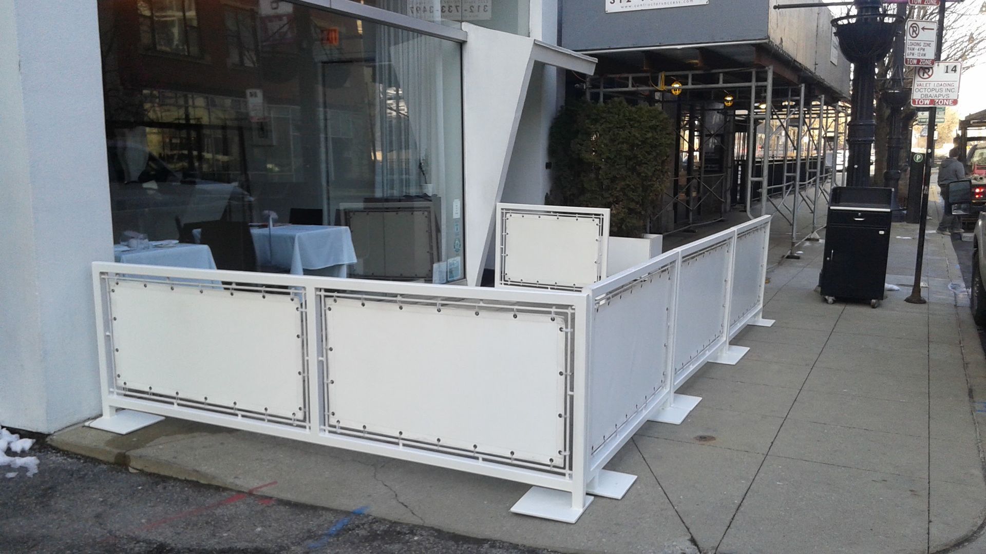 A white fence is sitting on the sidewalk in front of a restaurant.