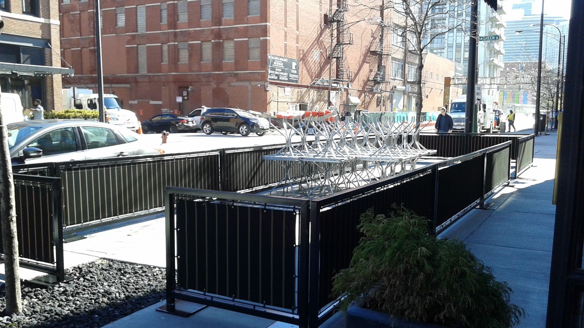 A fence along a sidewalk with a brick building in the background
