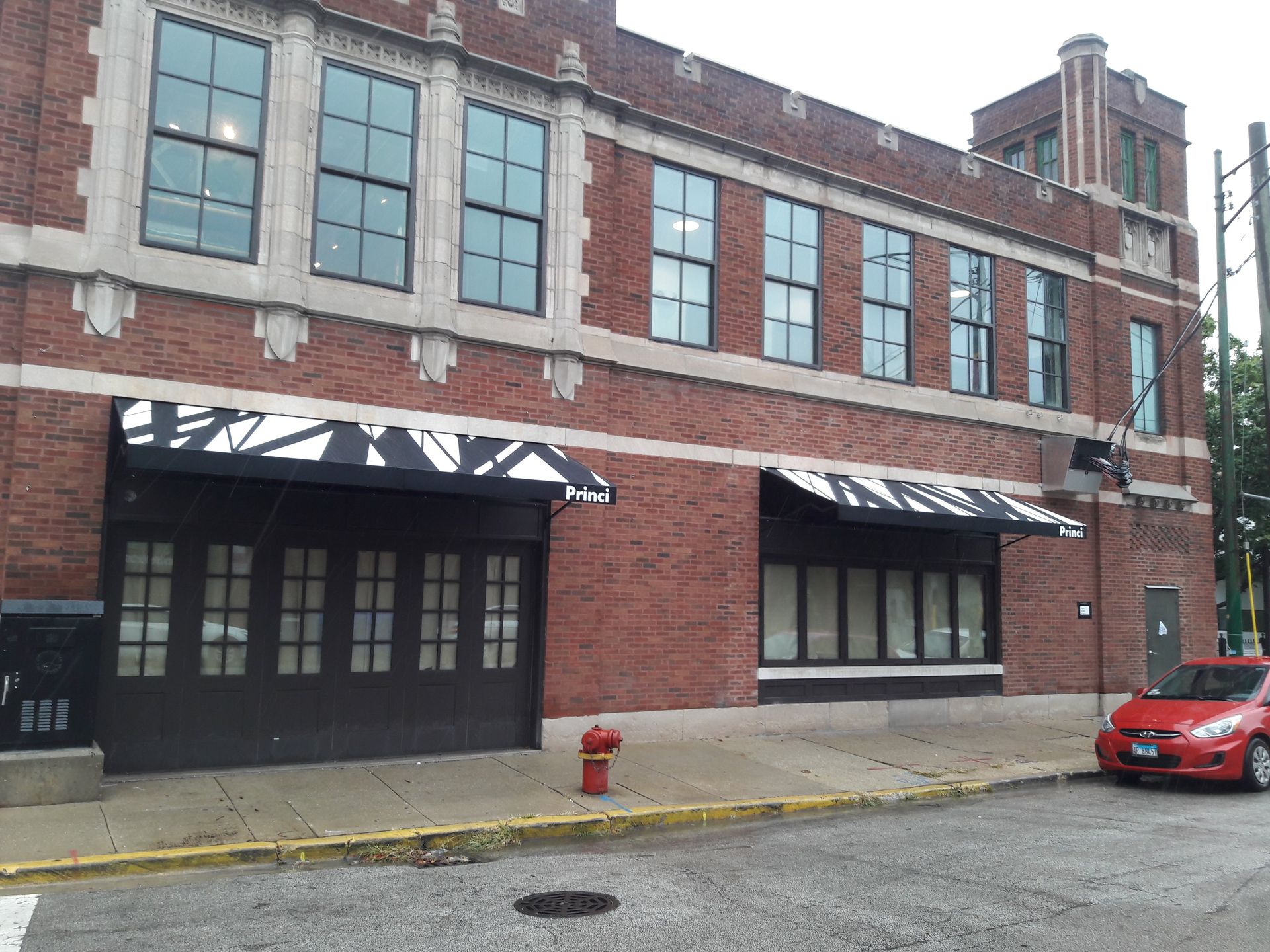 A red car is parked in front of a large brick building