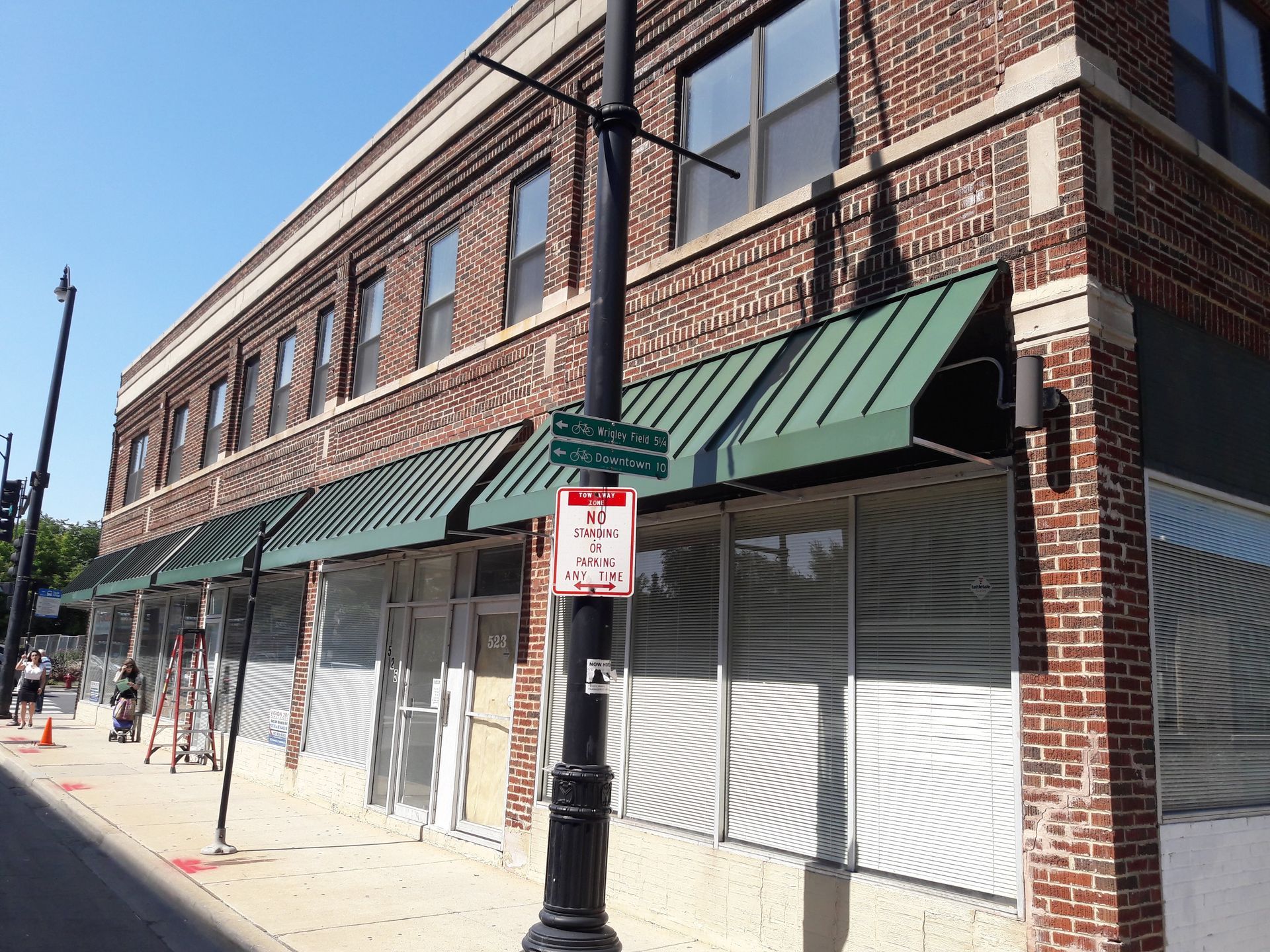A brick building with green awnings and a no parking sign