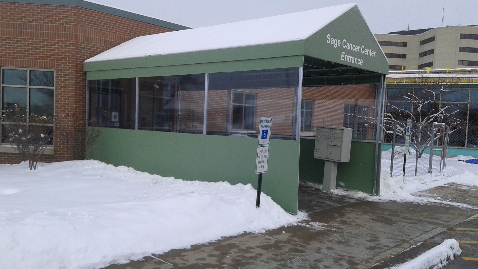 A green canopy is sitting in the snow in front of a building.