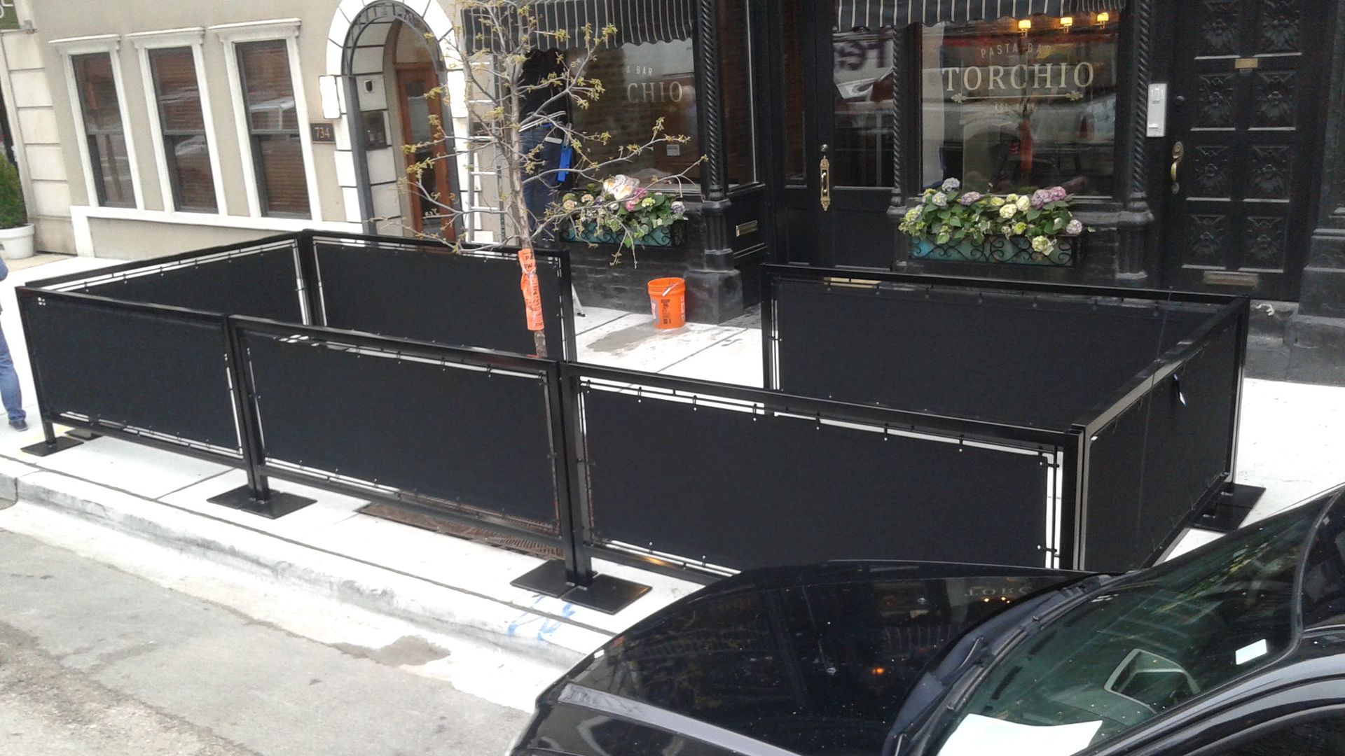 A black car is parked in front of a building with a black fence