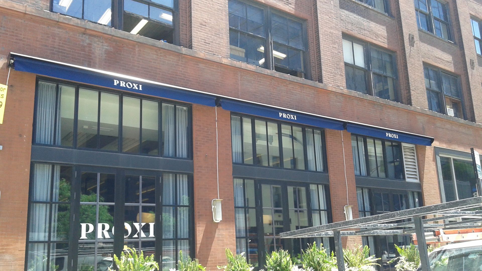 A brick building with a blue awning that says prosxi