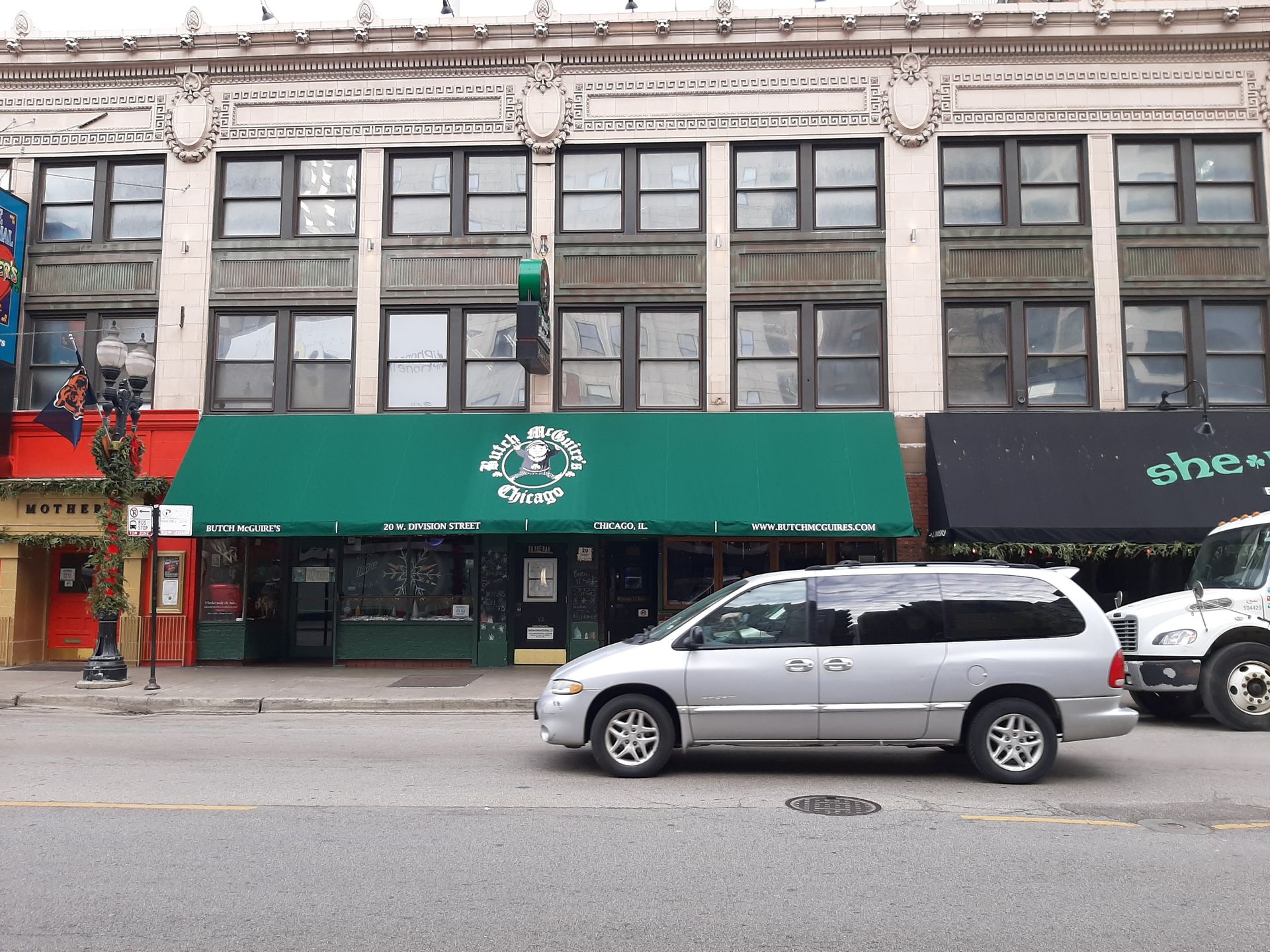 A silver minivan is parked in front of a building with a green awning