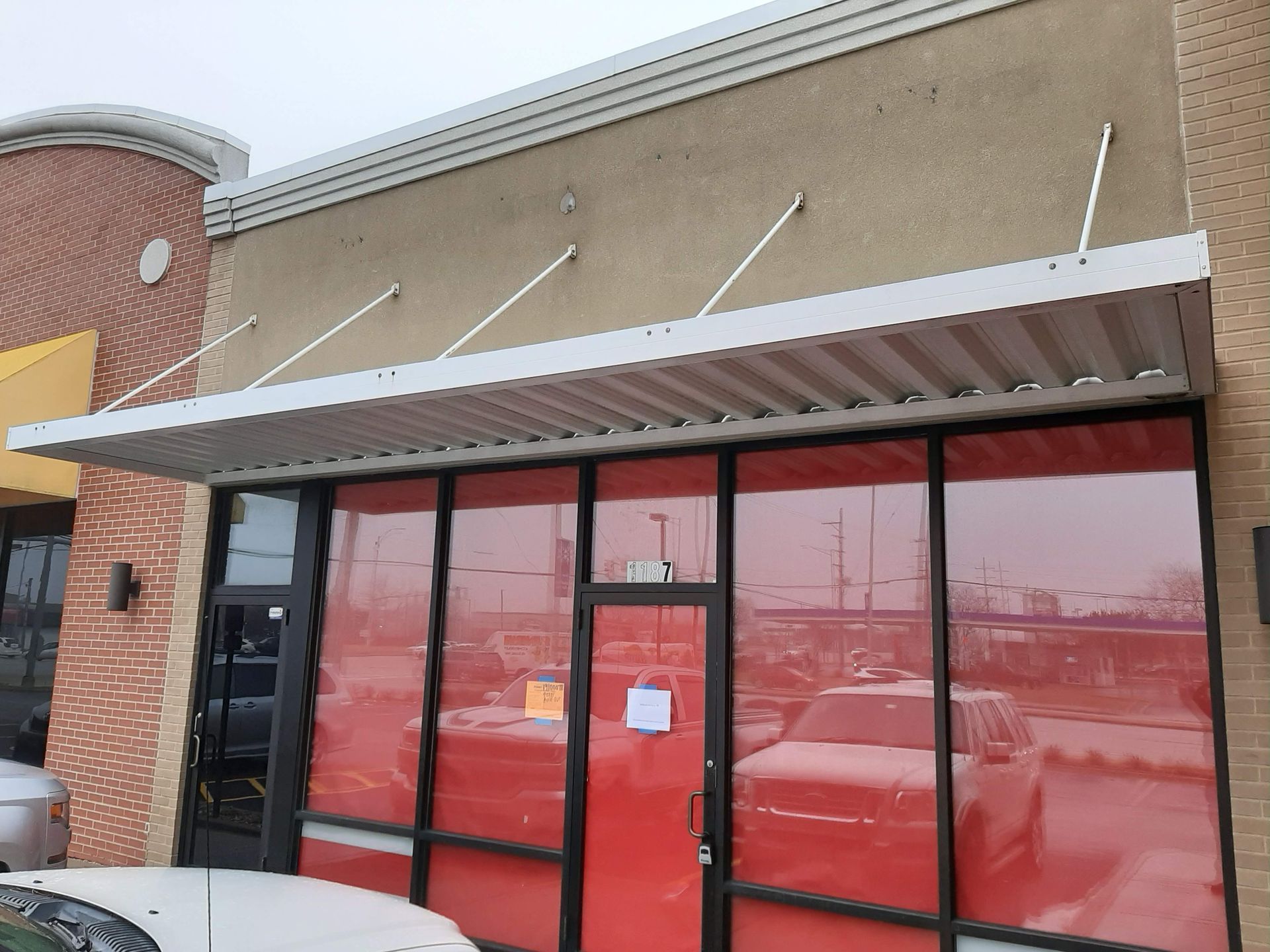 A white car is parked in front of a building with red windows