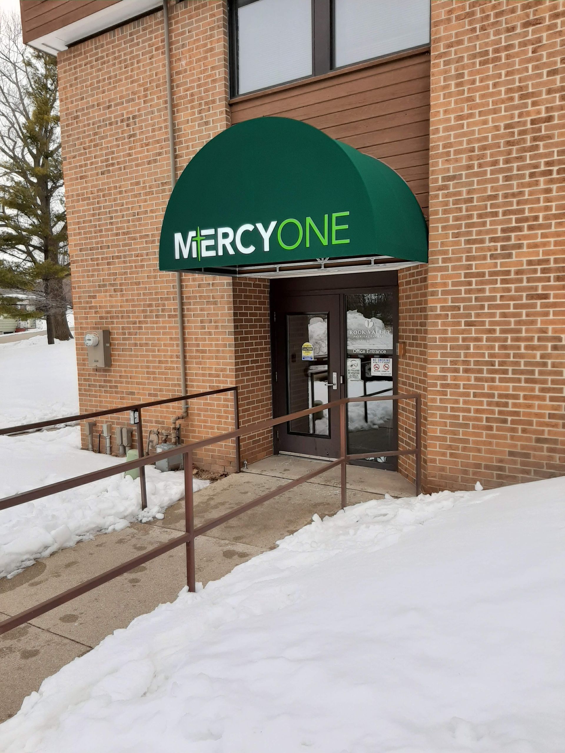 A brick building with a green awning over the door that says mercyone